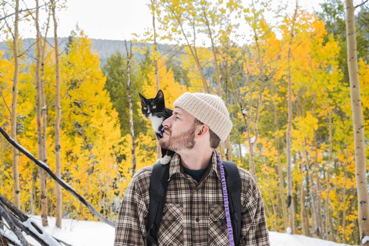 Dr. Sam Whitaker on a hiking trail with his tuxedo cat Penny riding on his shoulder